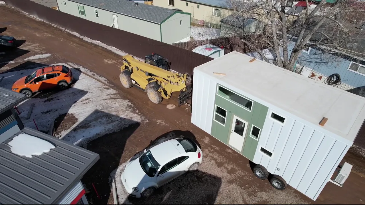 Delivered workforce housing unit with white metal panel siding, a green entry wall, and a glass-panel door