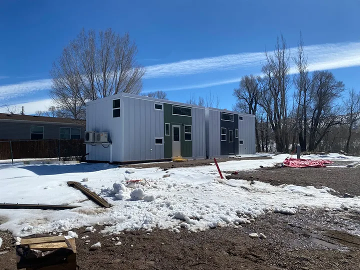 Two delivered workforce housing units with white panel siding and green and navy entry walls