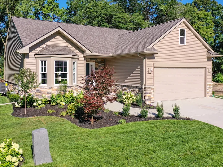Completed single-story home with tan siding, a stone base, a bay window, and an attached two-car garage
