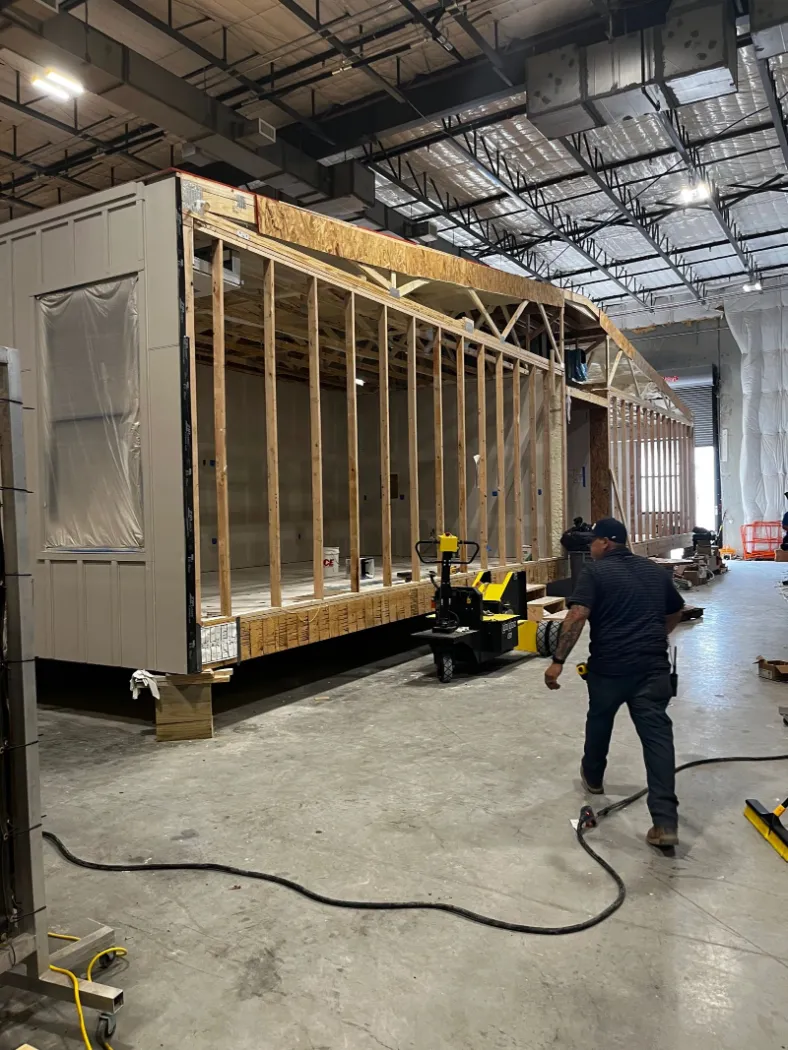 A framed module on the factory floor, with a worker alongside