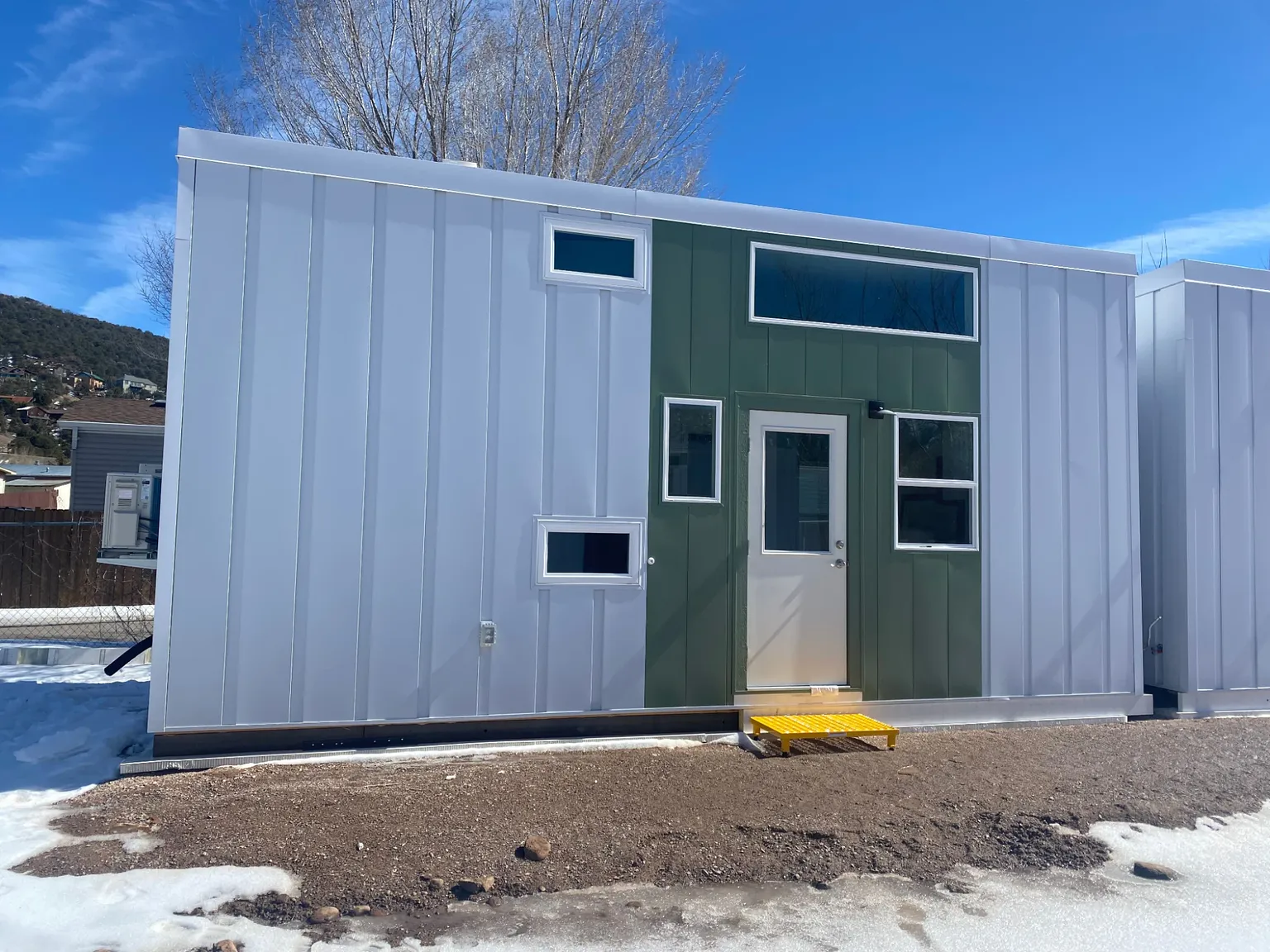 Workforce housing unit with white metal panel siding, a green entry wall, and a glass-panel door