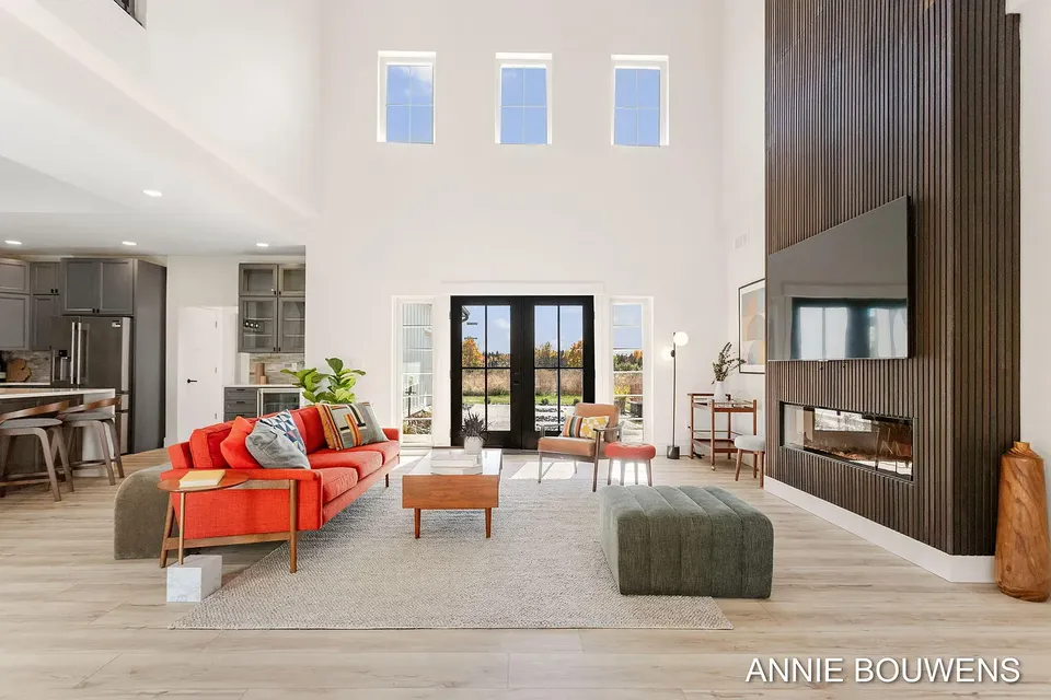 Two-story great room with a coral sofa, a slatted wood fireplace wall, and black French doors