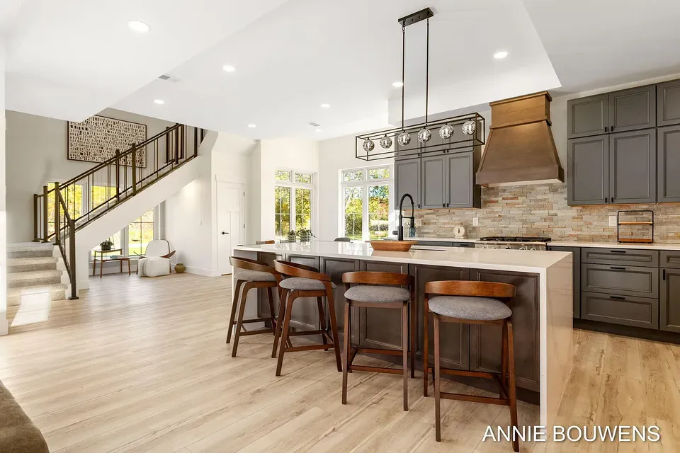 Kitchen with a long island, wood bar stools, a wood range hood, and an open staircase
