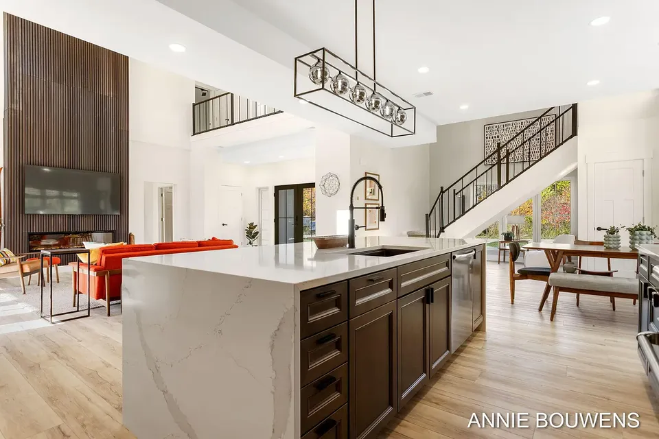 White waterfall-edge kitchen island with dark cabinets, a lantern pendant, and the staircase beyond