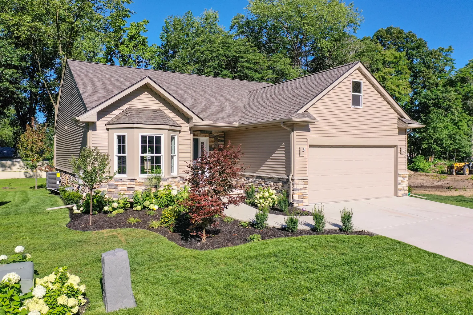 Completed single-story home with tan siding, a stone base, a bay window, and an attached two-car garage