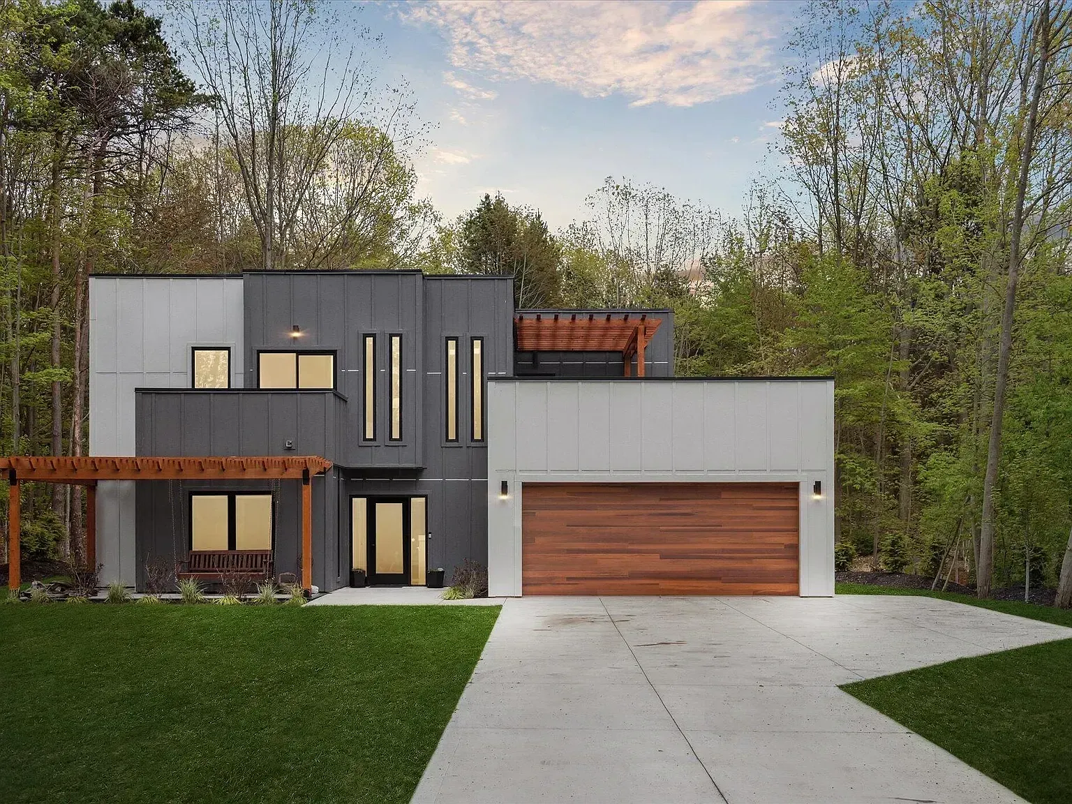 Modern flat-roof home with cedar garage door and pergola, set in the woods
