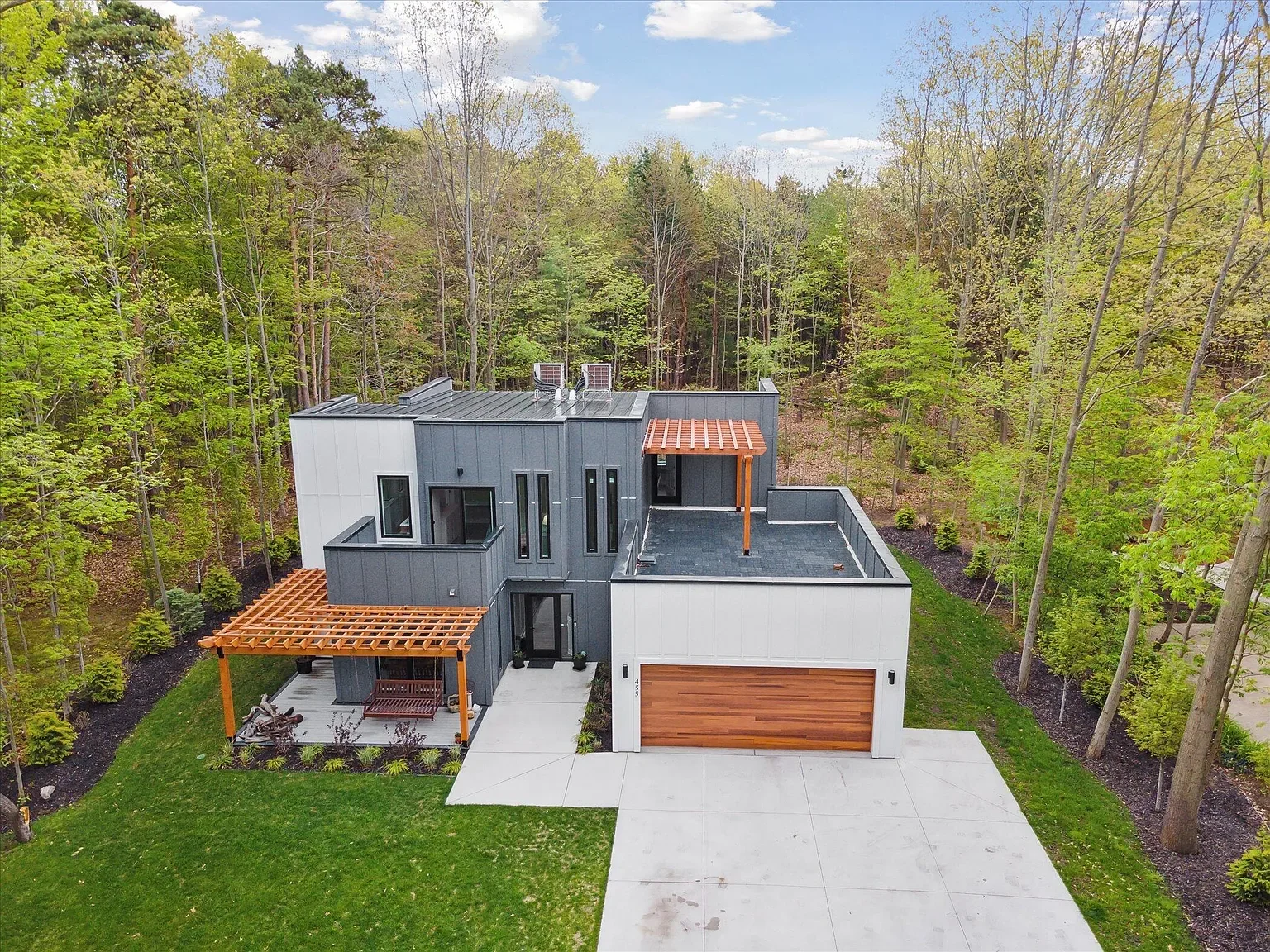 Aerial view of the home, rooftop deck, and wooded lot