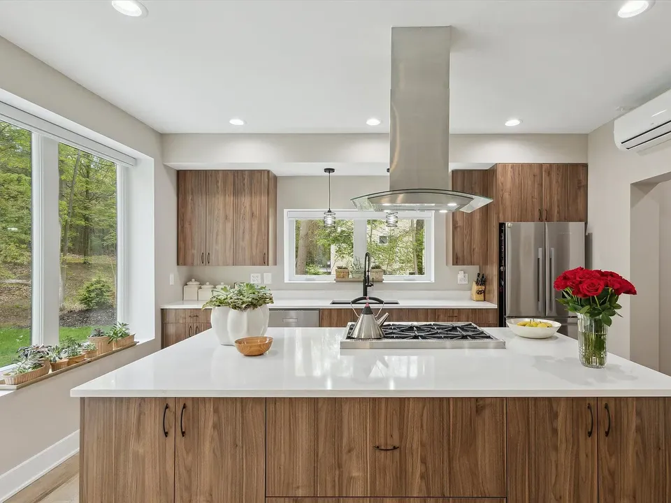 Kitchen with wood cabinetry, an island cooktop, and a stainless hood