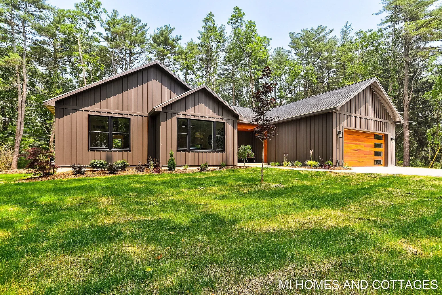 Dark board-and-batten modern farmhouse with cedar garage door, set among tall pines