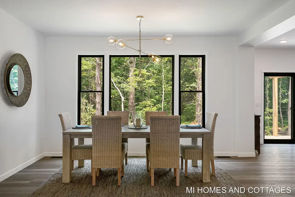 Dining room with a modern chandelier and black-framed windows facing the trees