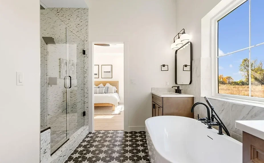 Bathroom with a freestanding tub, a glass shower, patterned floor tile, and a window onto open fields