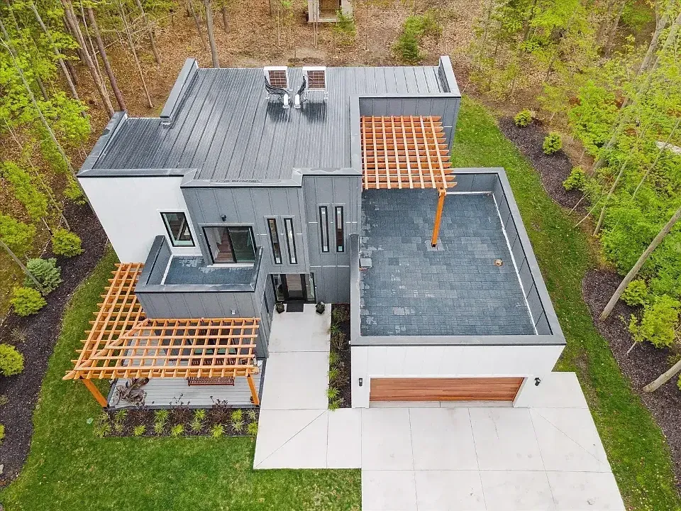Aerial view of a flat-roofed modern home with cedar pergolas, surrounded by trees