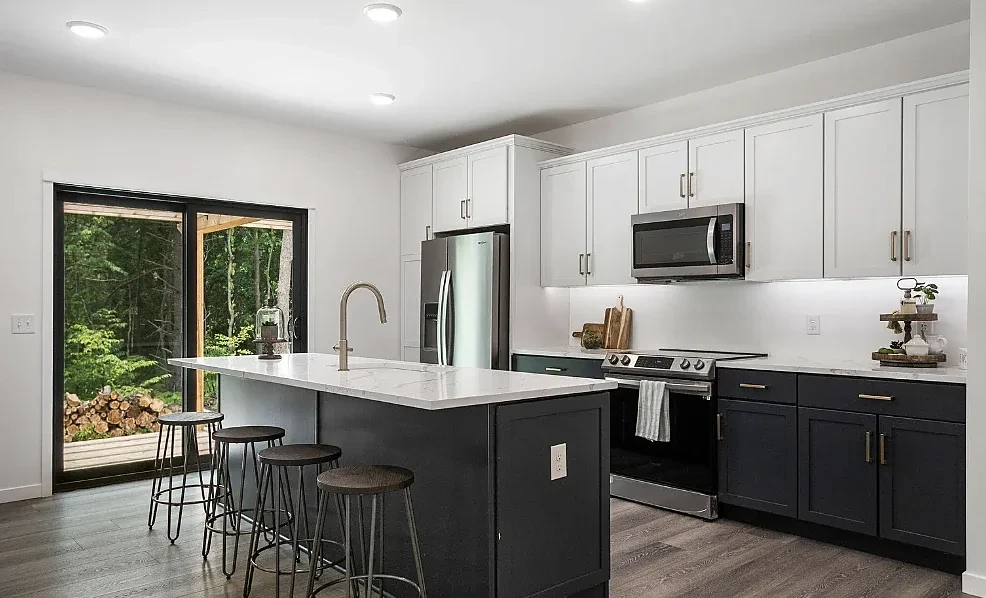 Kitchen with white upper cabinets, charcoal lower cabinets, a marble-look island, and a sliding door to a wooded deck