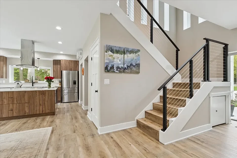 Open interior with a cable-rail staircase, light wood floors, and a walnut kitchen