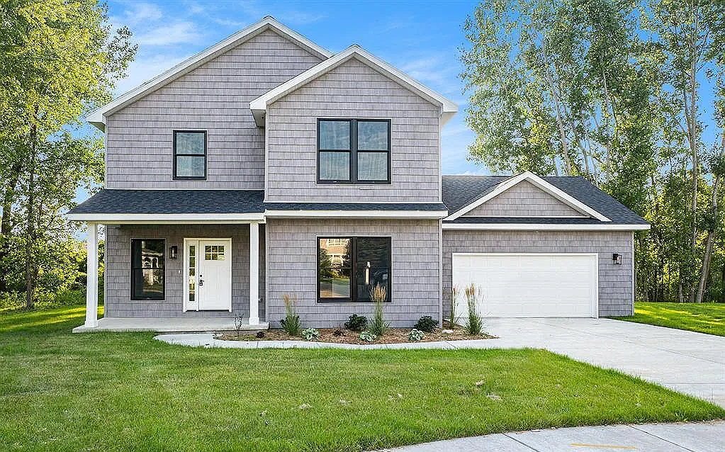 Completed two-story home with gray shingle siding, a covered front porch with white columns, and an attached two-car garage