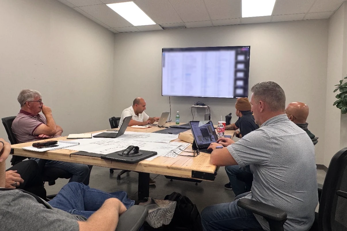 The Papaya team around a conference table covered in floor plans, working through a project on laptops and a wall screen