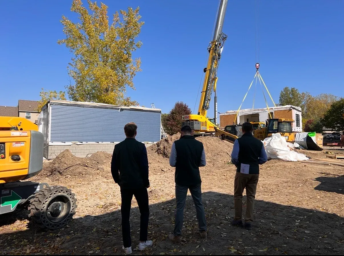 Three members of the team on a job site, watching a crane lift a module into place beside a completed first section