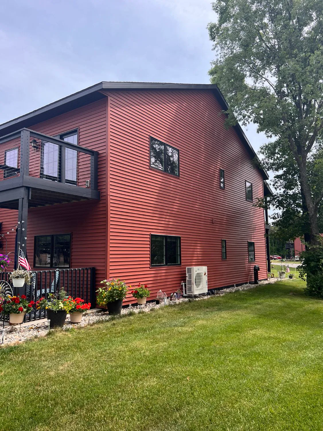 Side of a Twin Oaks building with red siding, a balcony above the patio, and a mini-split unit on the lawn
