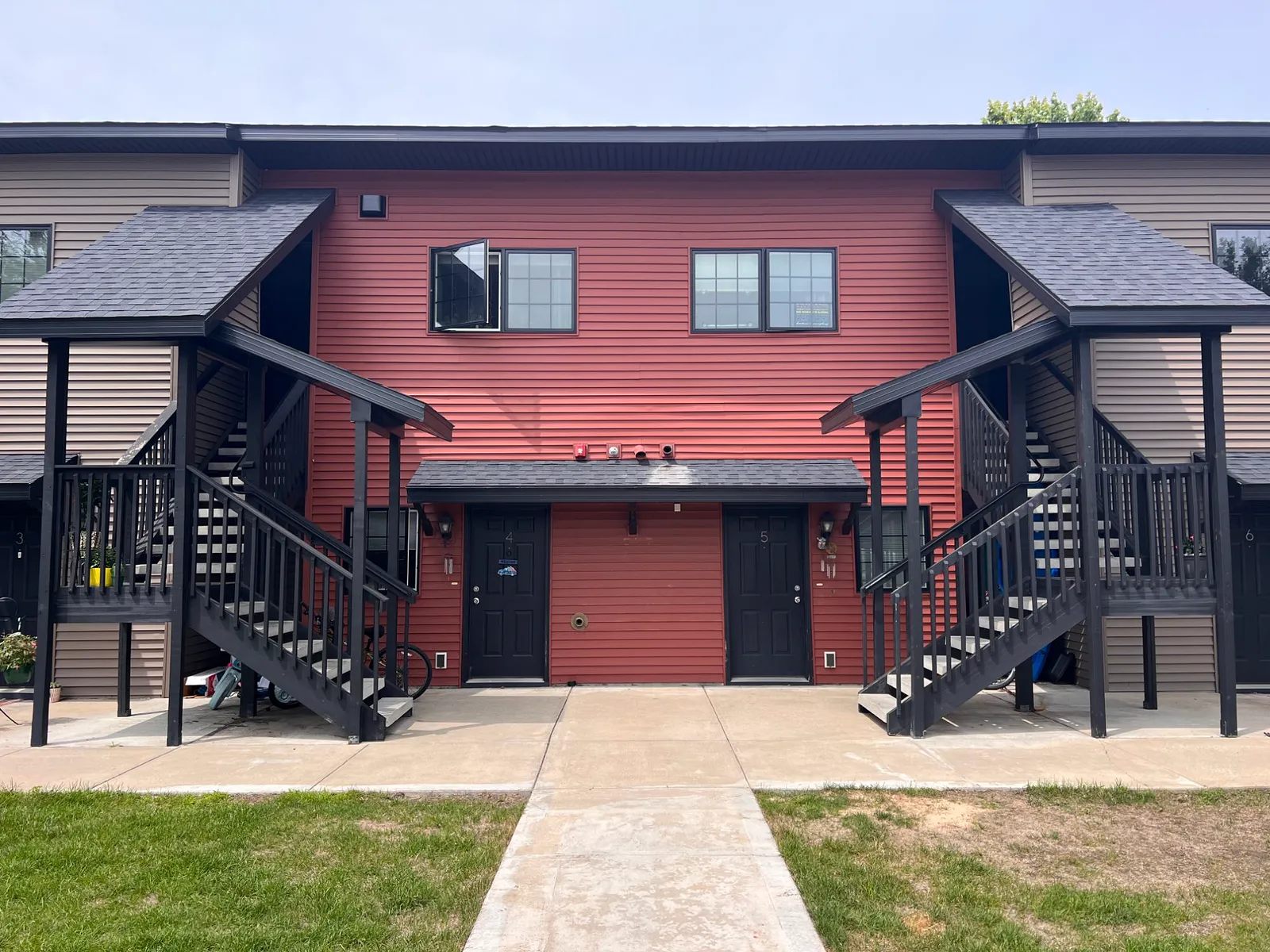 Front of a Twin Oaks building: red siding between two covered black exterior stairs, with ground-floor entries