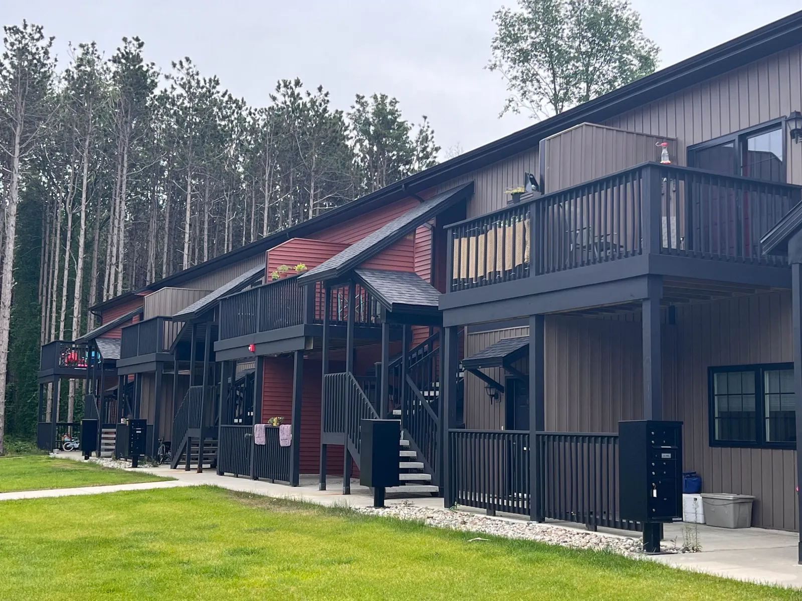 Row of Twin Oaks buildings with covered stairs and balconies, set against tall pines