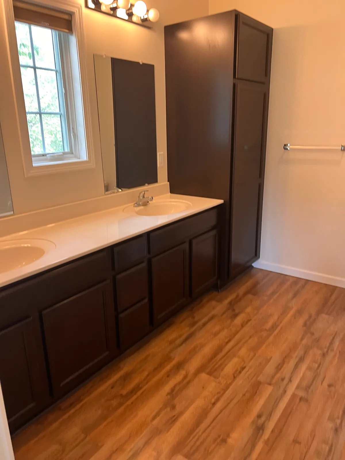 Bathroom with a double-sink vanity, a tall linen cabinet, and wood-look flooring
